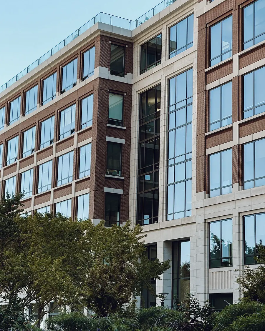 A low-rise modern office building with tall windows, seen from the street behind trees.