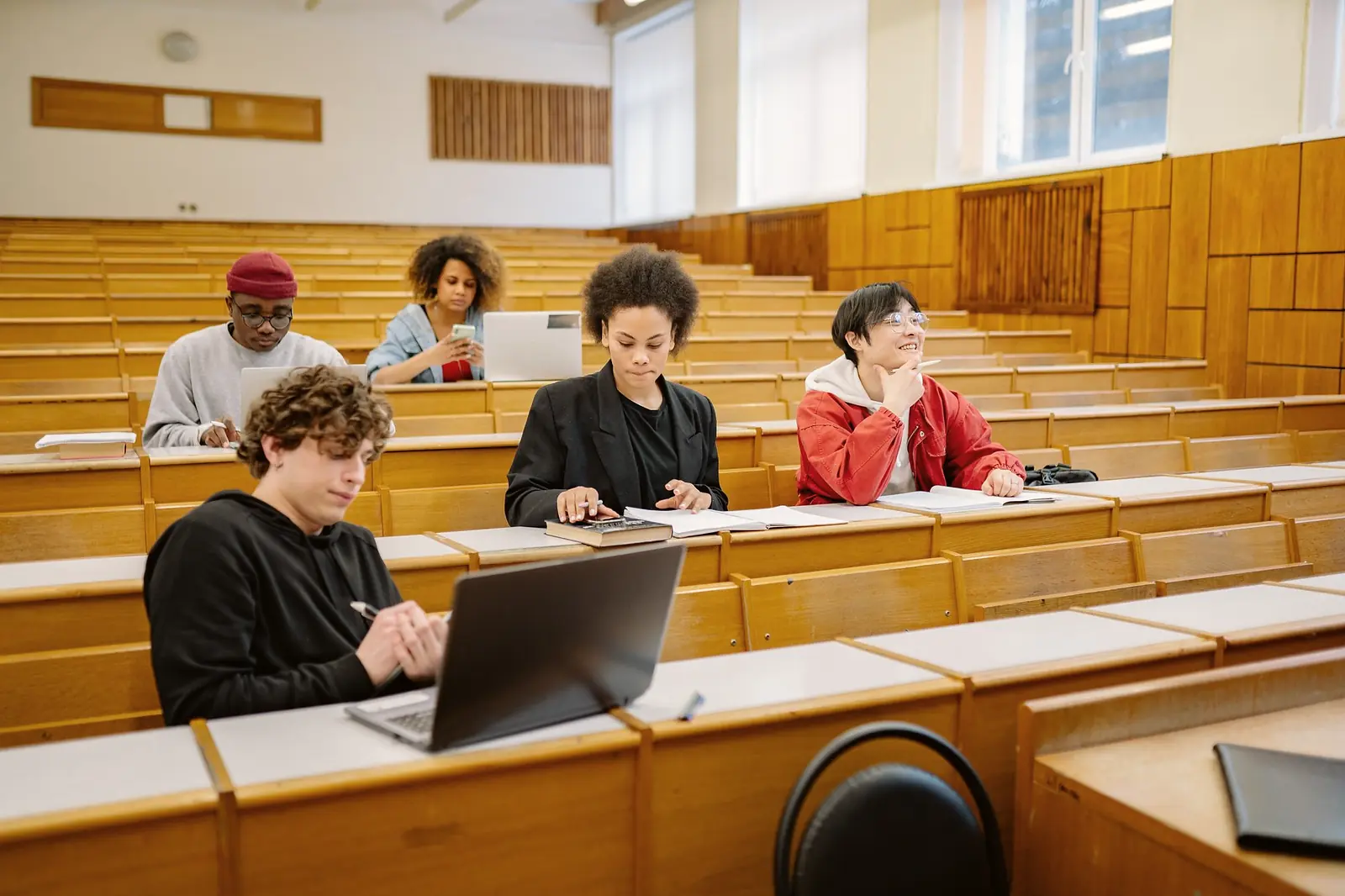 Students working through material at laptops on the tiered desks of a lecture hall.