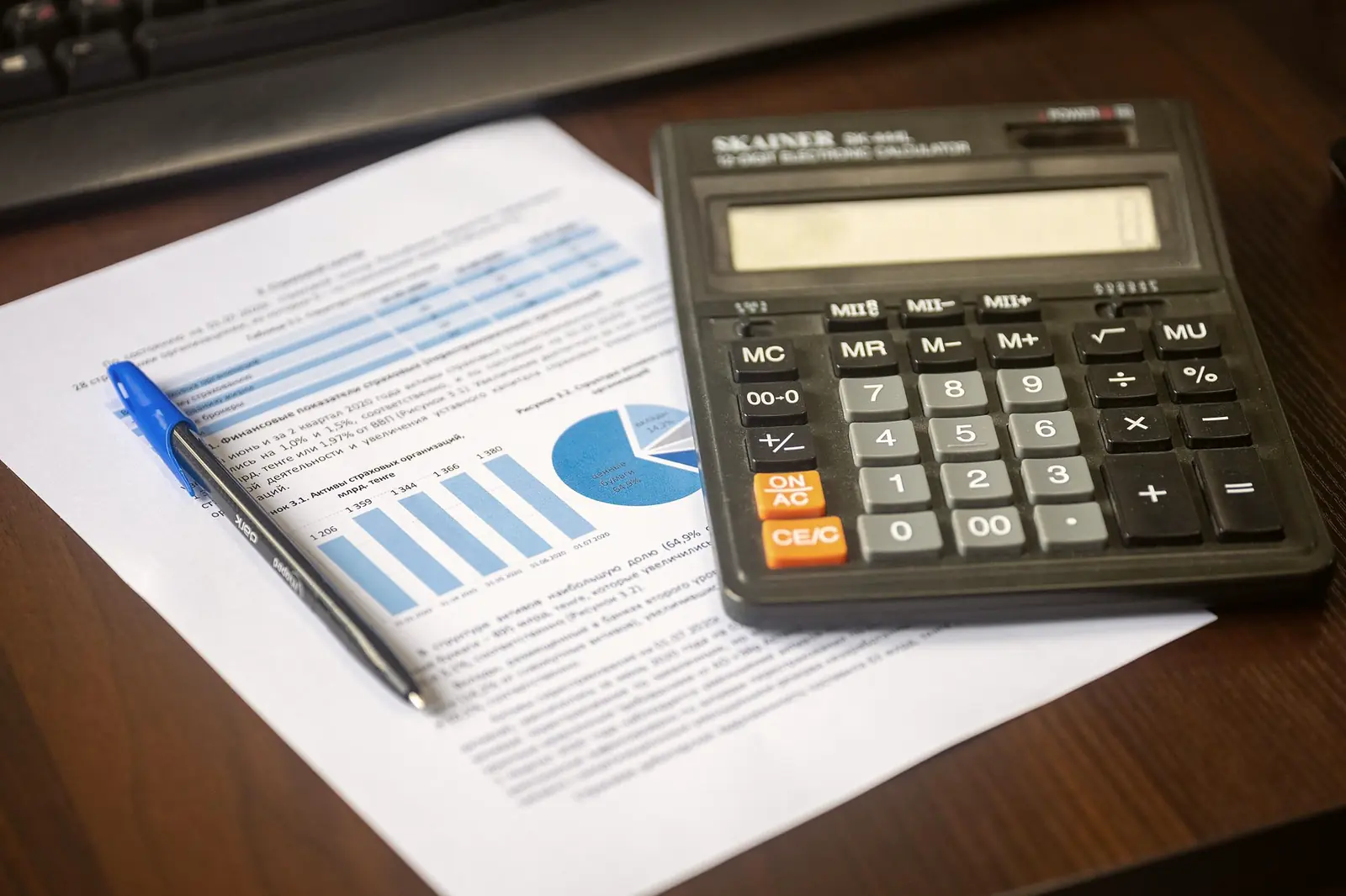 A desk calculator and a pen resting on a printed report of bar and pie charts.